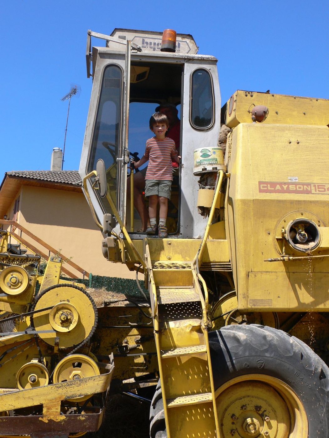 A young child sitting at the controls in the cab of a yellow excavator.