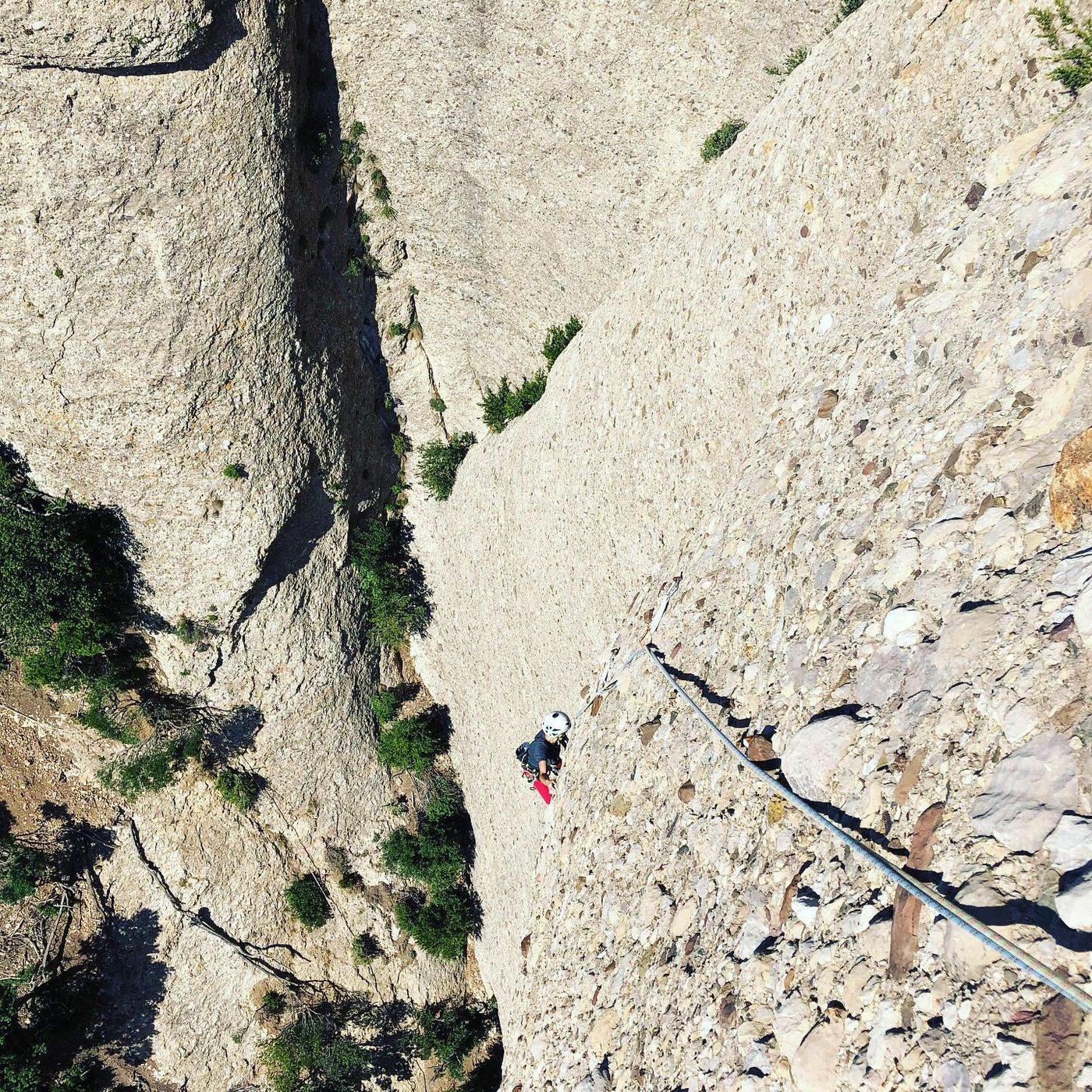 Looking down a steep limestone face, with climbers strung out along the route below.