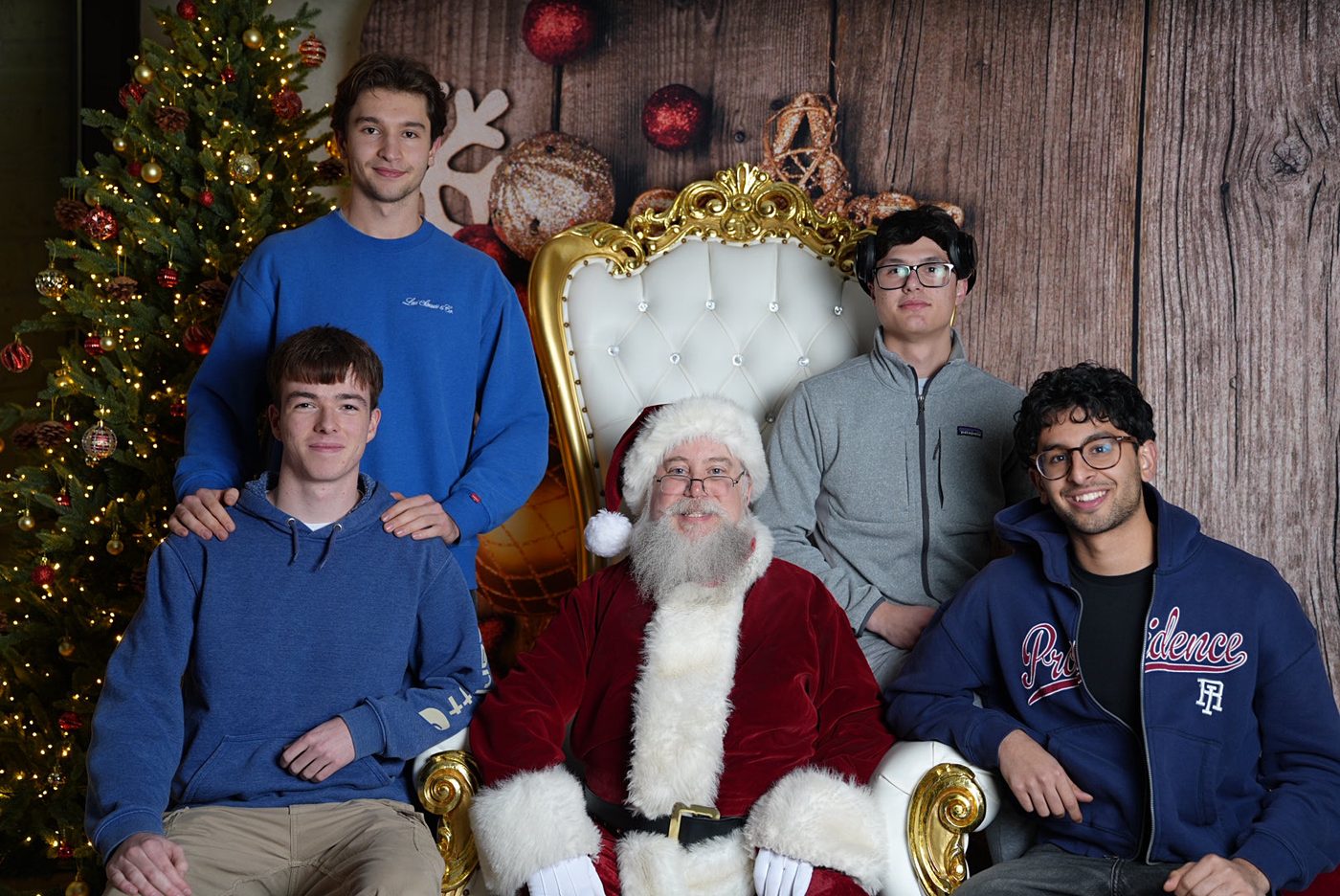 Four friends posing either side of a Santa in front of a Christmas tree.