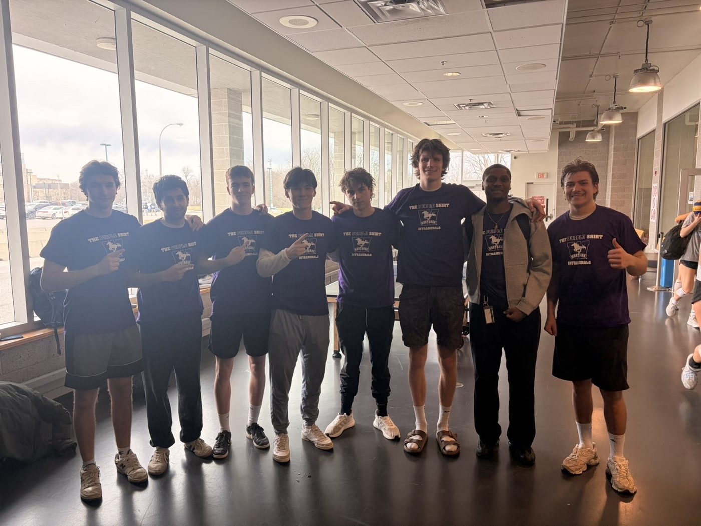 A team in matching shirts lined up along a bright, glass-walled corridor.