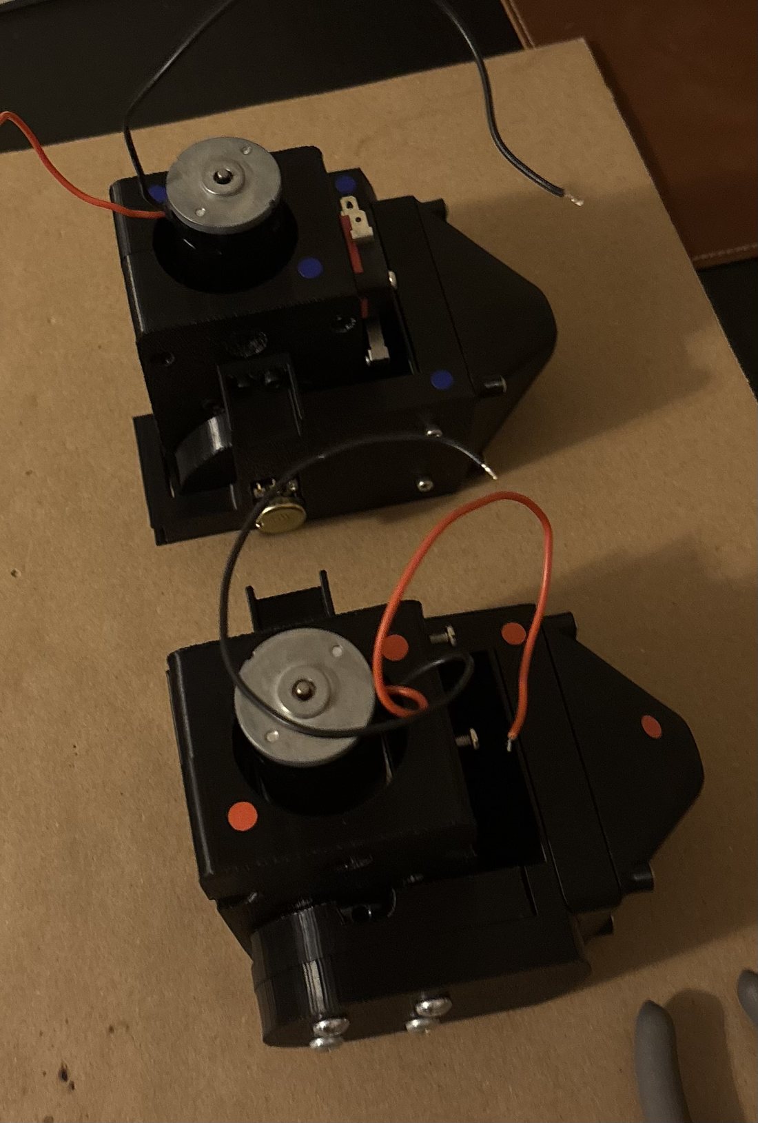 Two assembled black 3D-printed elbow modules with gear motors and wiring, sitting on a workbench.