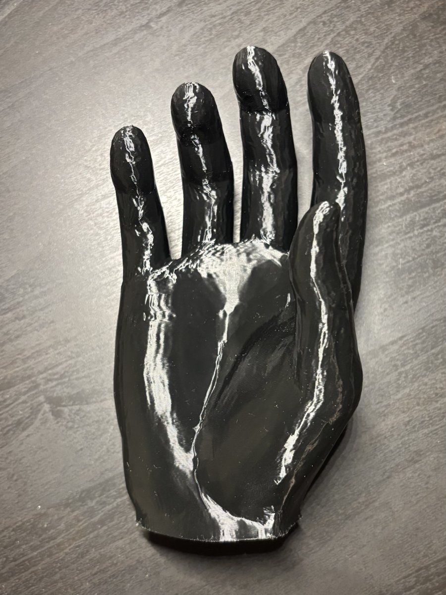 3D-printed black hand, palm side up, showing individually printed fingers and a seam across the palm.