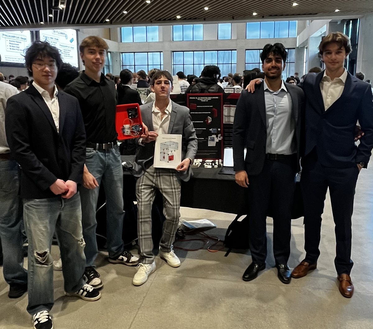The five-person Flush Factory team standing in front of their competition display, one member holding the red filtration unit and another holding the printed build manual.