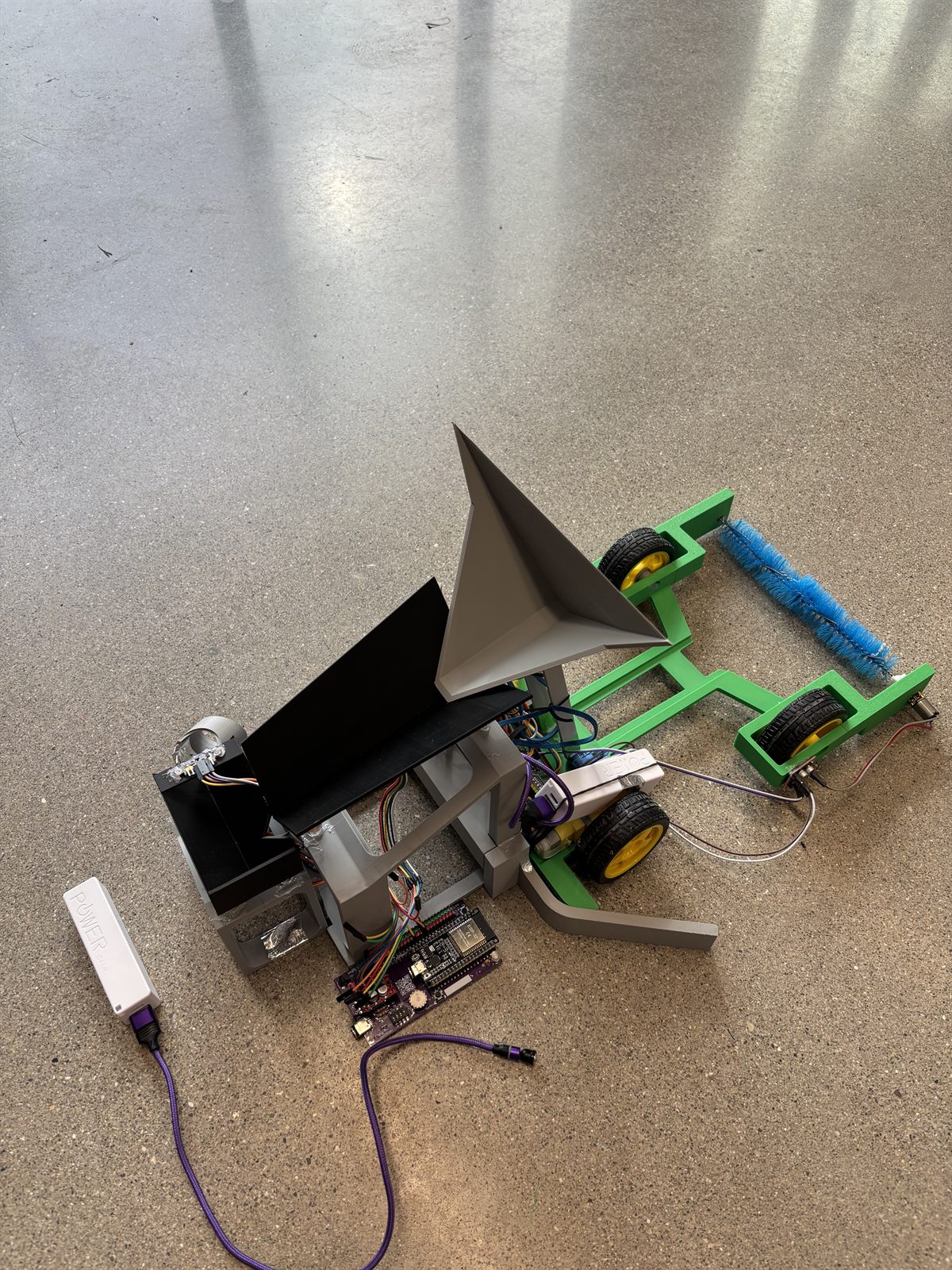 The scavenger robot reversed into the sorting station with its scoop tipped up, emptying erasers onto the sorter's black inclined platform.
