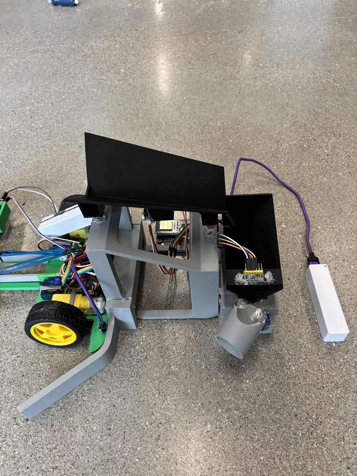 Close view of the sorting station showing the grey printed frame, the black inclined feed platform, the colour sensor board mounted at the chute mouth, and the grey diverter tube below.